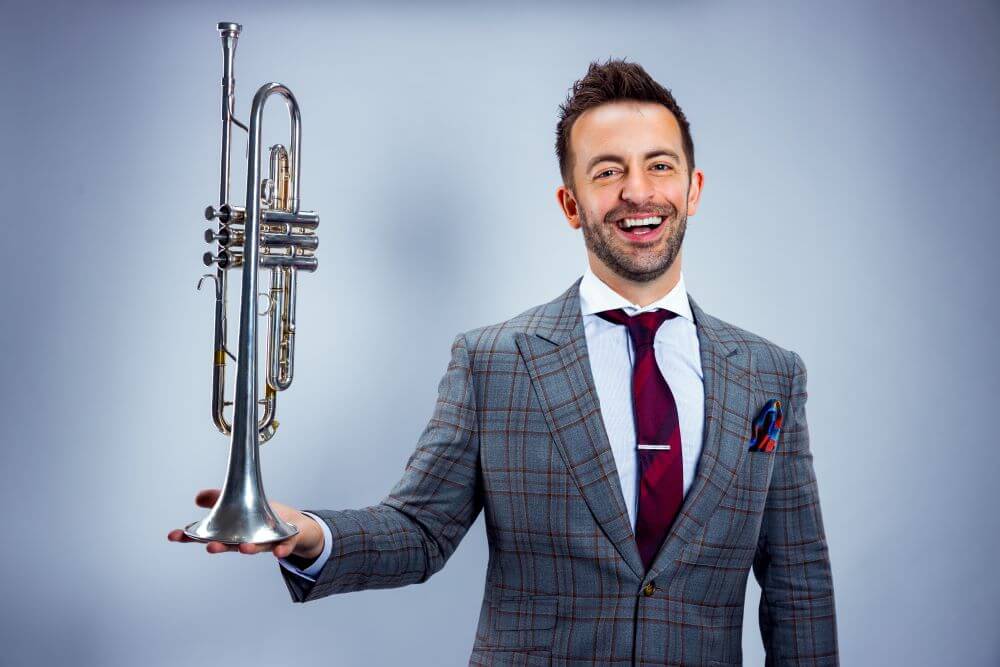 photo of a smiling benny benack playfully holding a trumpet