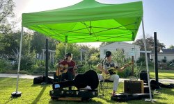 bryce janey and david schroder playing guitar under a tent at james alan mcpherson park