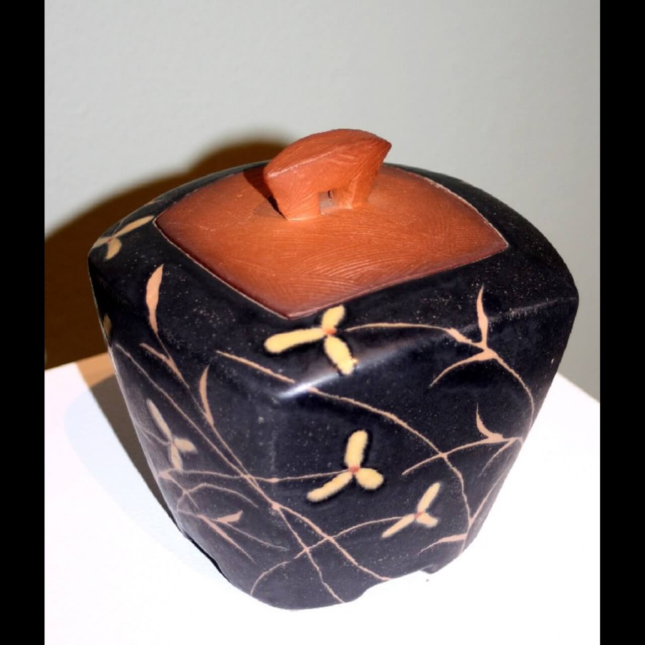 square jar made of red clay and decorated with floral design in black gaze